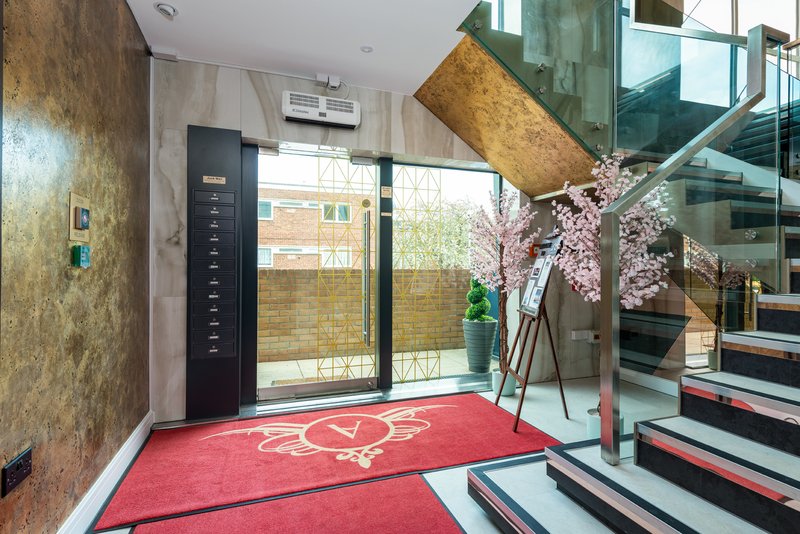 Modern building entrance with red carpet, glass doors, decorative flowers, and staircase visible