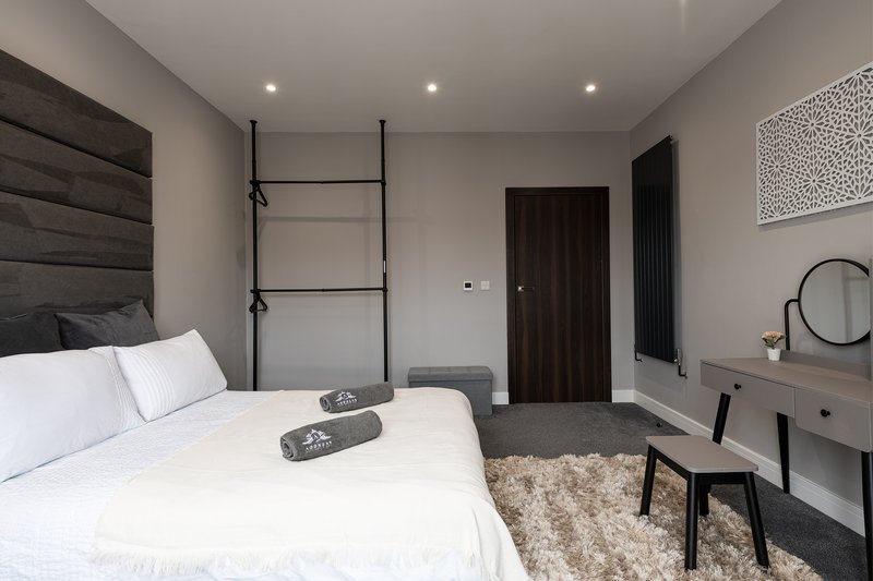 Modern bedroom with double bed, black headboard, ladder shelf, dark doors and contemporary furnishings