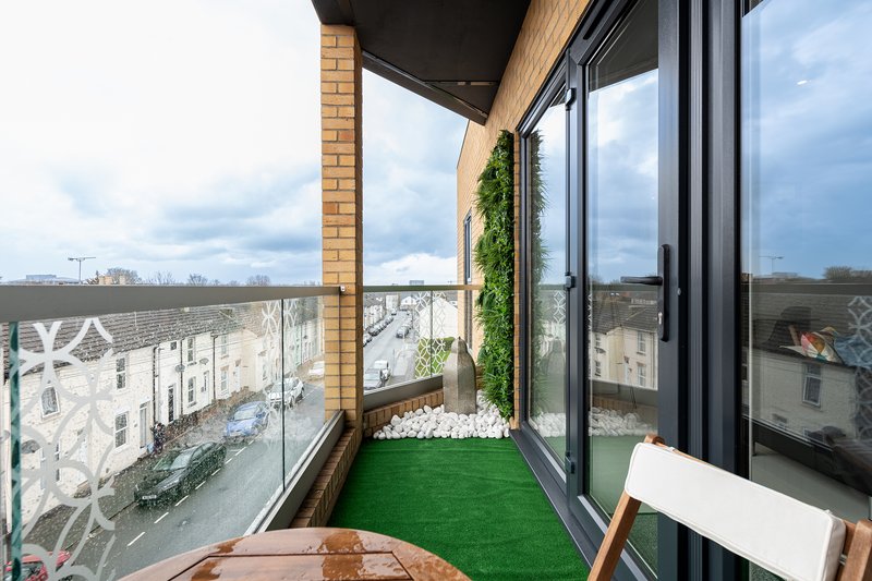 Elevated balcony with artificial grass, green climbing plant, and views over residential buildings