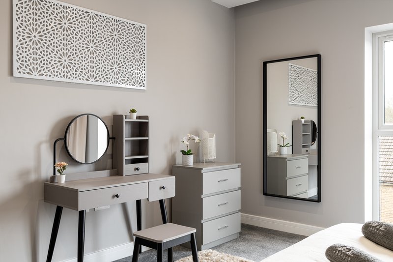 Modern bedroom with vanity desk, round mirror, chair, and full-length mirror on wall