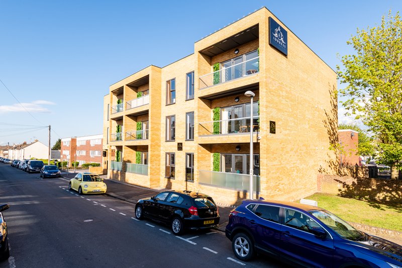 Modern yellow-brick apartment building with balconies, street view and parked cars