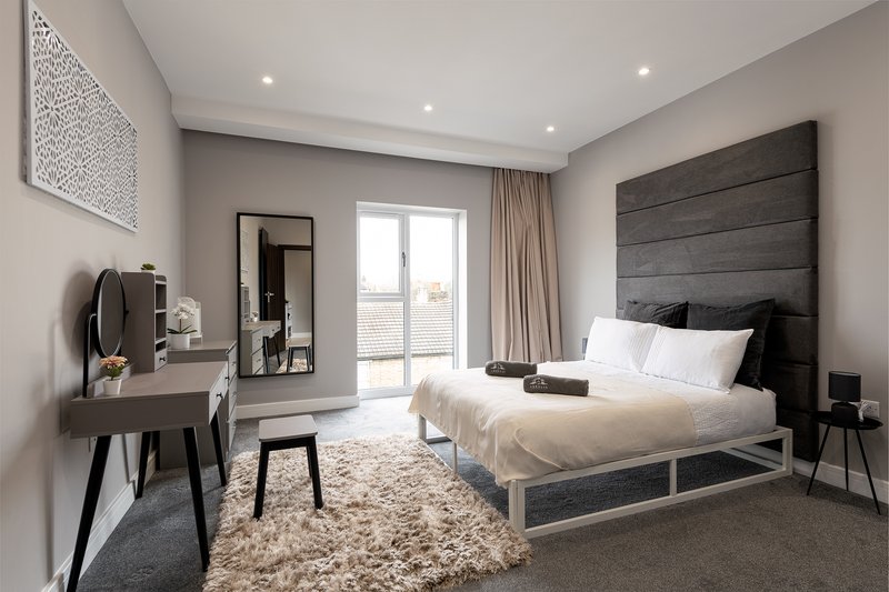 Modern bedroom with double bed, wooden headboard, desk, and floor-to-ceiling windows