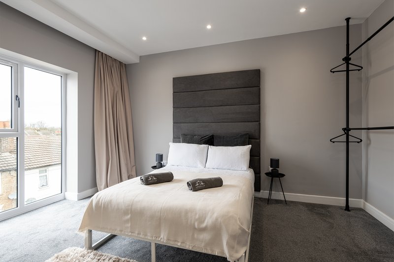 Modern bedroom with grey upholstered headboard, cream bedding, and floor-to-ceiling windows