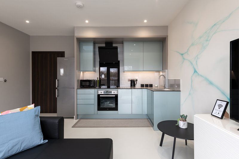 Modern open-plan kitchen and living area with light blue cabinetry, stainless steel appliances, and black seating