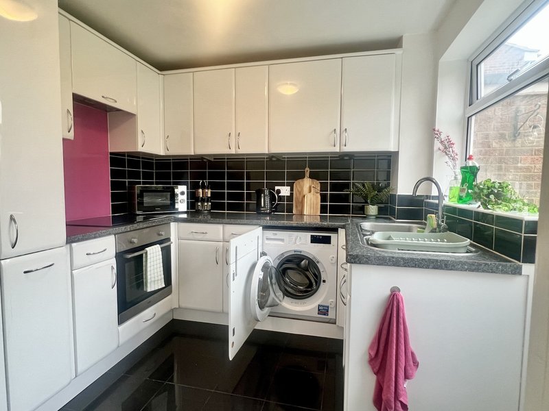 Modern kitchen with white cabinets, black tile backsplash, integrated appliances and washing machine
