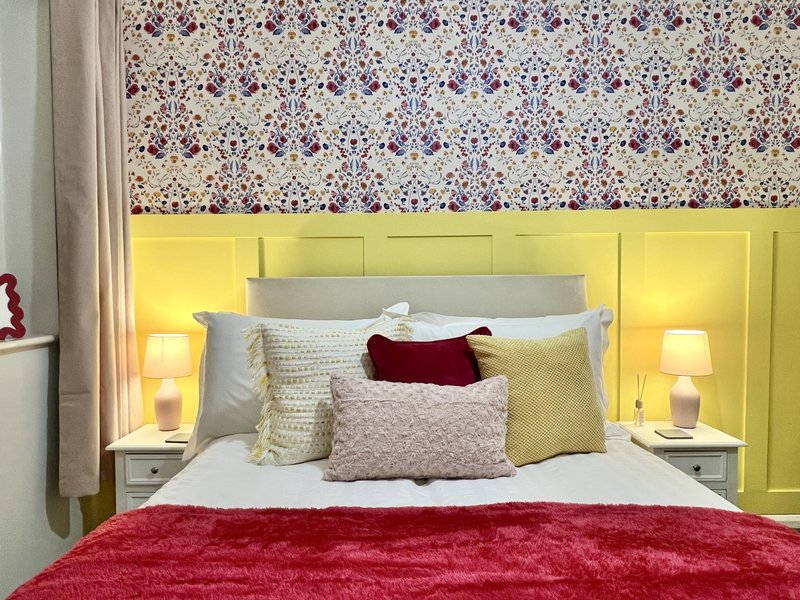 Bright bedroom with yellow headboard, patterned wallpaper, and red velvet bedding