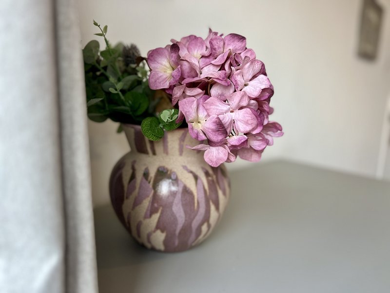 Purple hydrangea flowers in ceramic vase on white shelf