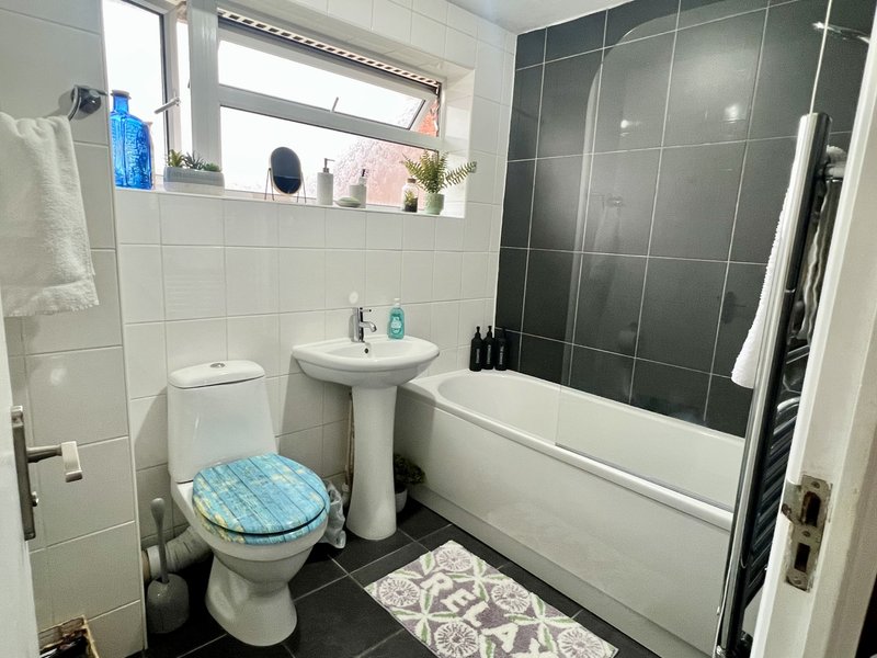 Clean bathroom with toilet, pedestal sink, bathtub with shower enclosure and window
