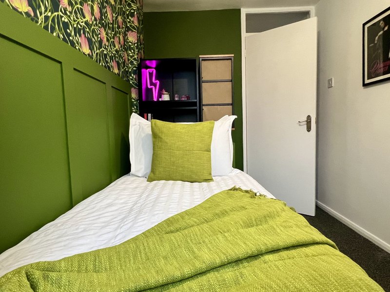 Modern bedroom with green accent wall, double bed with lime bedding, white pillows and shelving unit
