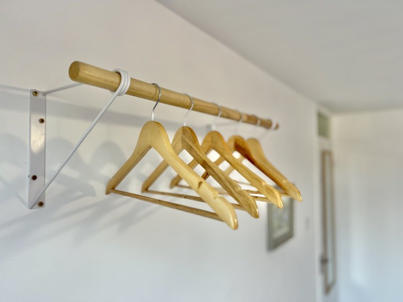 Wall-mounted wooden clothing rail with five empty wooden hangers in bedroom
