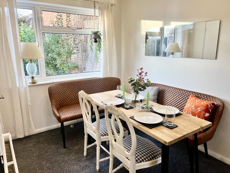 Dining area with wooden table, upholstered brown bench seating, white chairs and large window with garden view