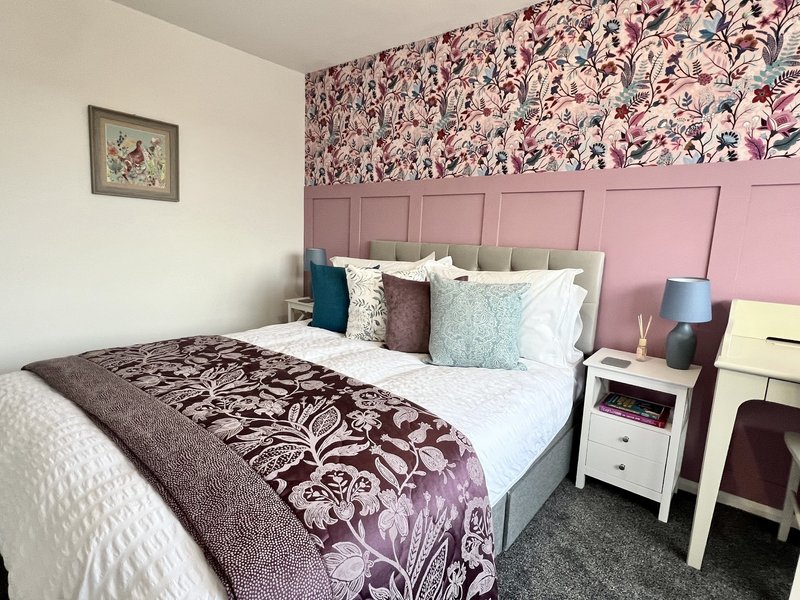 Bedroom with double bed, pink headboard, floral wallpaper, and bedside furniture