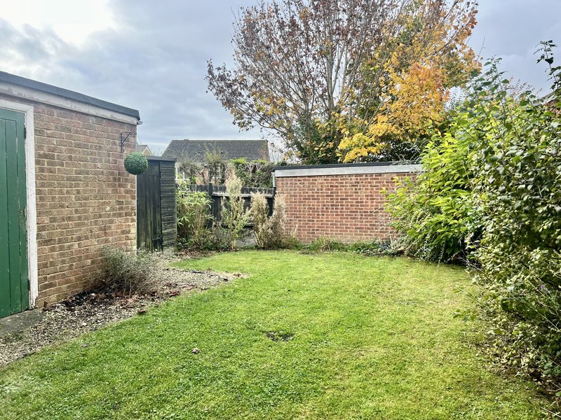 Enclosed garden with lawn, brick walls, green gate and mature trees