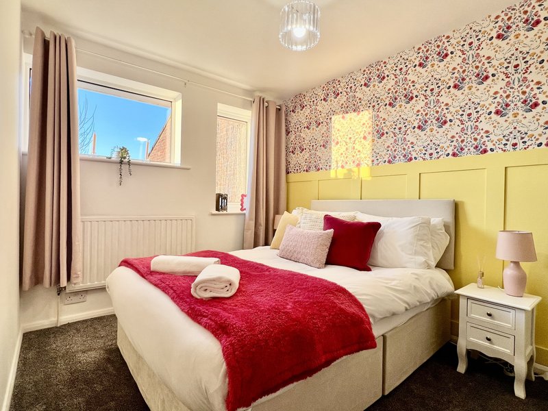 Bright bedroom with double bed, yellow headboard, floral wallpaper, and window with blue sky view