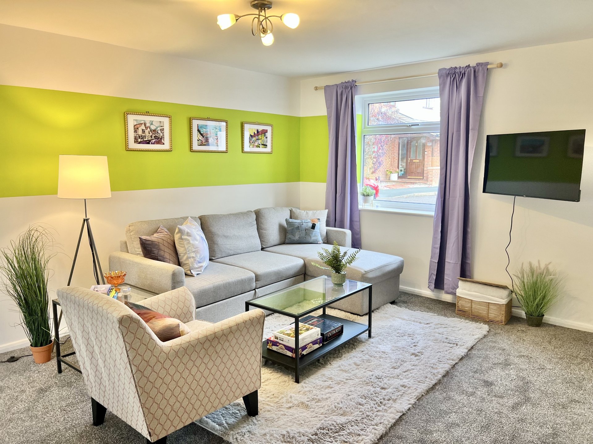 Bright living room with lime green accent wall, grey sofa, cream armchair, and wall-mounted TV