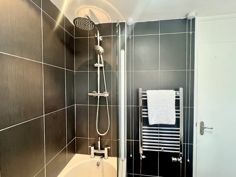 Modern bathroom with dark tile shower enclosure, rainfall showerhead, white towel rail and folded towels