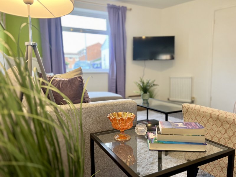 Bright living room with cream seating, patterned armchair, coffee table, plants and wall-mounted TV