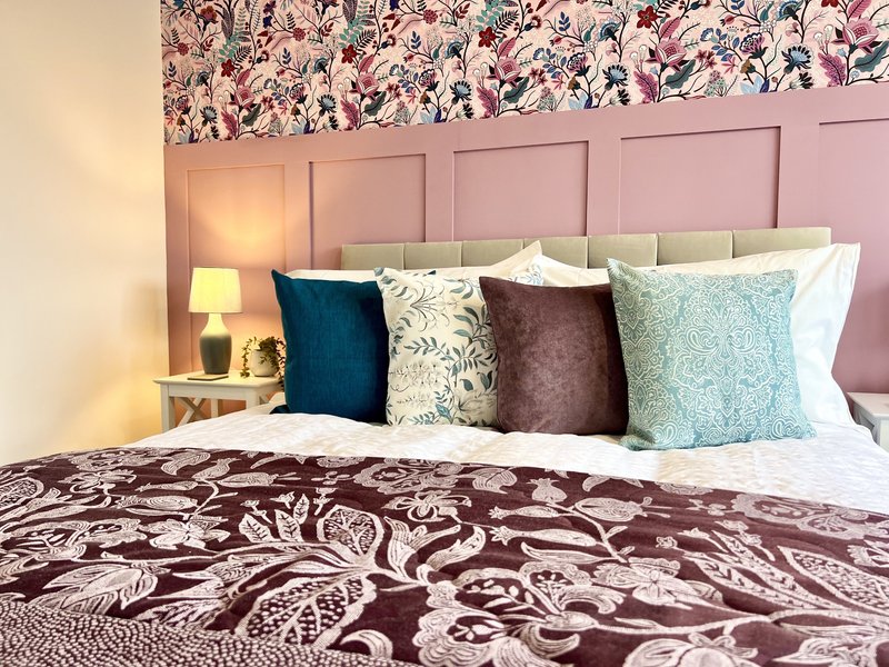 Bedroom with upholstered headboard, decorative pillows, patterned bedding and bedside lamp