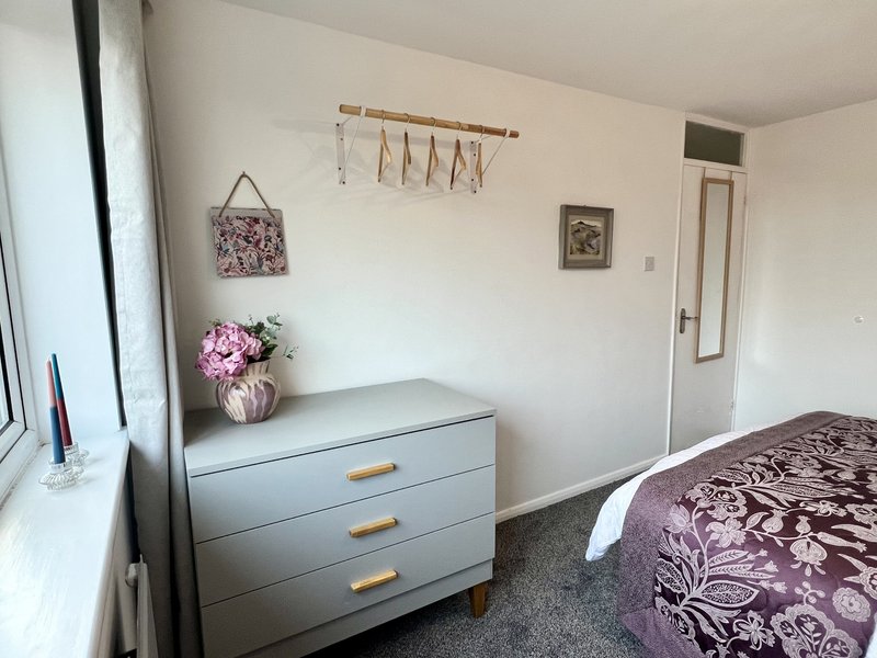 Bedroom with grey dresser, pink flowers, wooden wall organizer, and patterned bedding