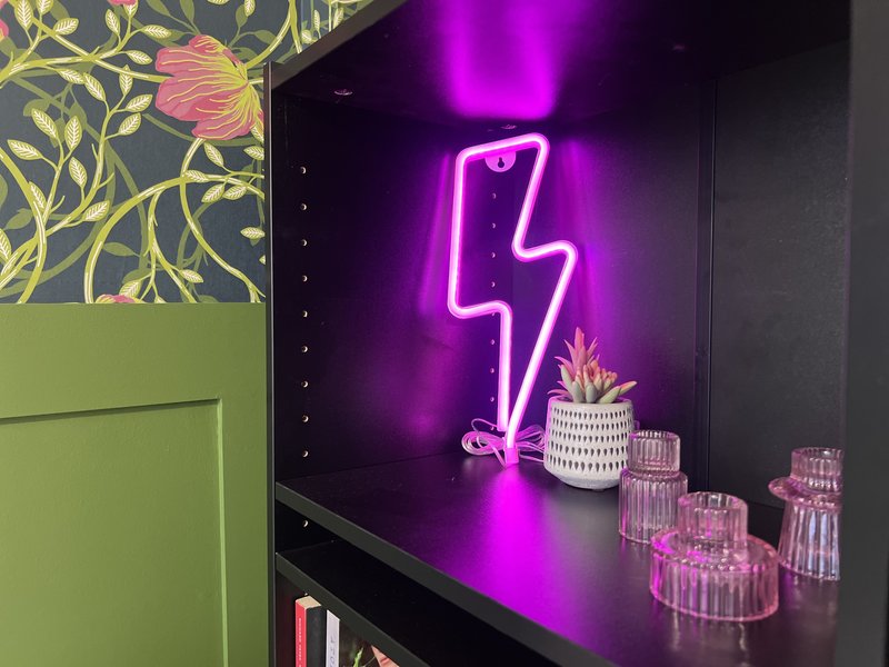 Interior shelving with neon lightning bolt sign, decorative plants and pink glass candle holders