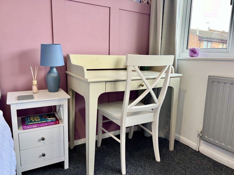 Bedroom workspace with cream desk, white chair, small bedside table and pink accent wall