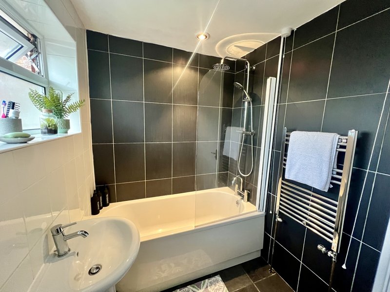 Modern bathroom with black tile walls, white bathtub, shower screen, and heated towel rack