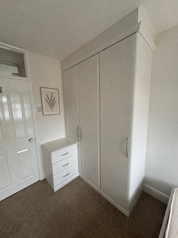 Bedroom with white wardrobe, chest of drawers, door, and brown carpet flooring
