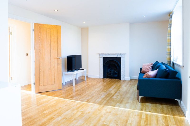 Spacious living room with wooden flooring, fireplace, blue sofa and television