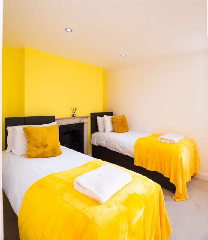 Bright bedroom with three single beds, yellow headboards, yellow bedding and cushions, white pillows