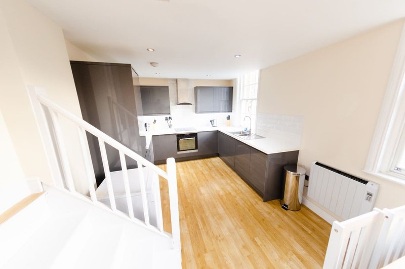 Modern kitchen with dark cabinetry, wooden flooring, white staircase and dining area