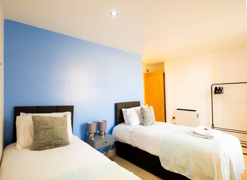 Bright bedroom with two single beds, blue accent wall, wooden flooring and yellow door
