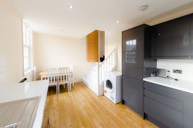 Open-plan kitchen and dining area with wooden flooring, white walls, dark cabinetry, and staircase