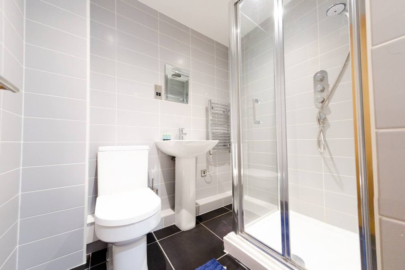 Modern bathroom with white toilet, sink, shower enclosure and dark floor tiles