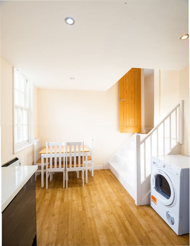 Open-plan living space with wooden dining table, chairs, washing machine and staircase
