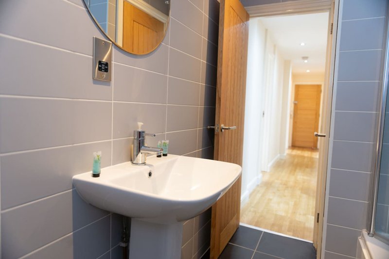 Modern bathroom with pedestal sink, round mirror, wooden vanity and grey tile walls
