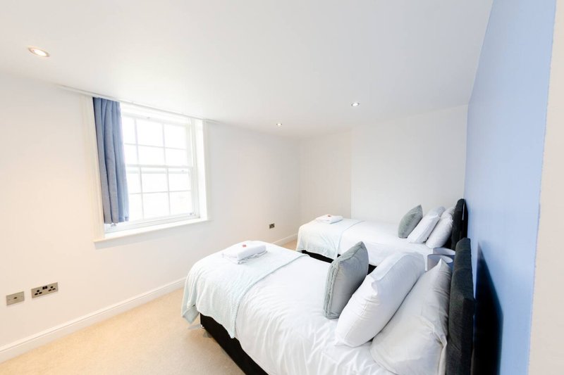 Bright bedroom with two single beds, white bedding, grey headboard and blue accent wall