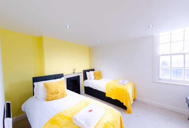 Bright bedroom with two single beds, yellow accent wall, white bedding and yellow cushions