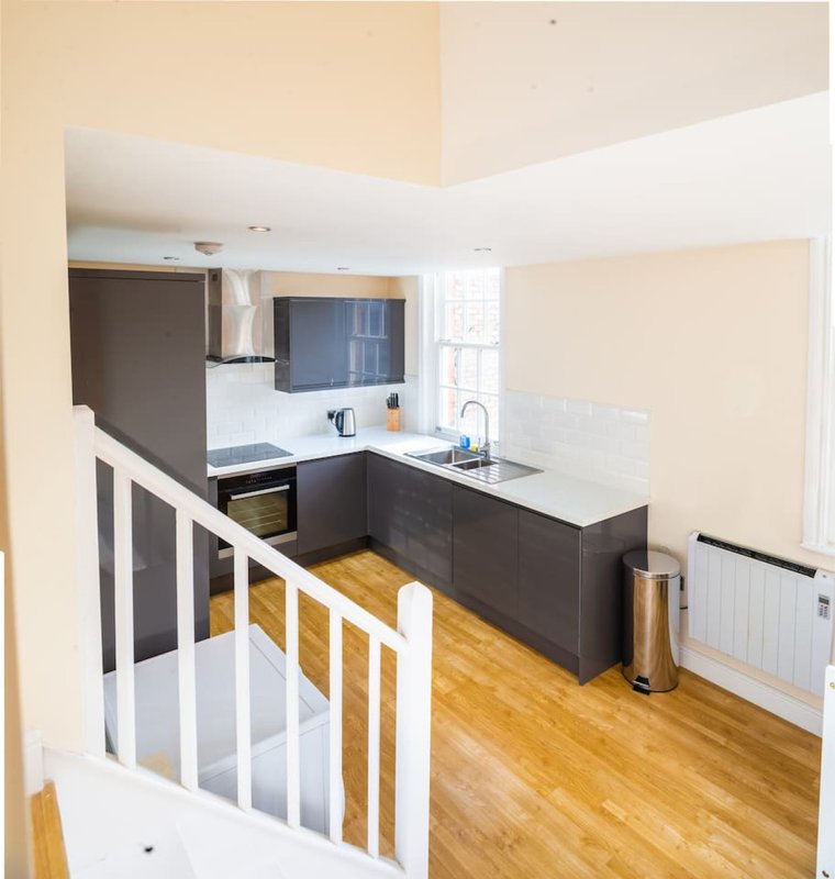 Modern kitchen with dark cabinetry, white countertops, wooden flooring and staircase railing