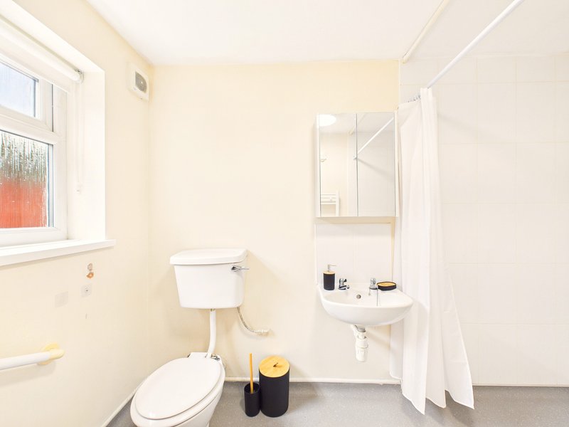 Small bathroom with toilet, wall-mounted sink, shower enclosure and window