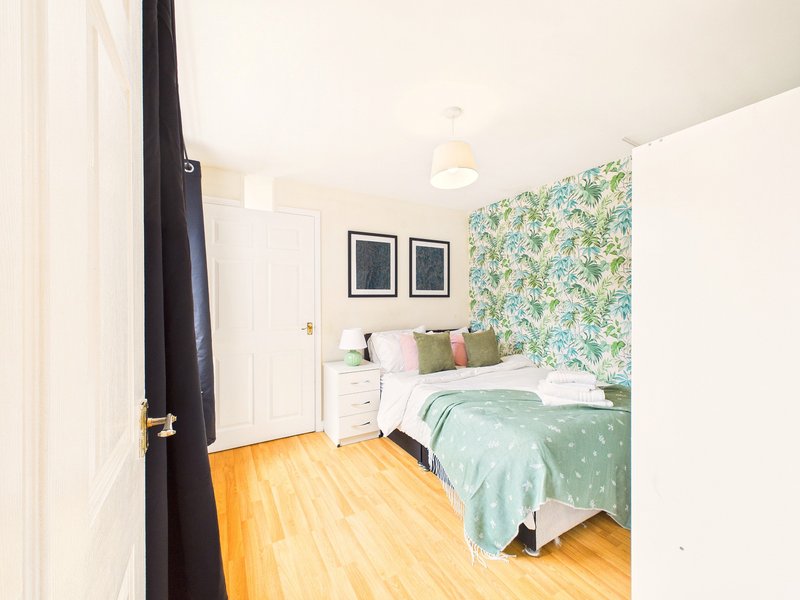Bright bedroom with double bed, green bedding, floral headboard, wooden floor and pendant light