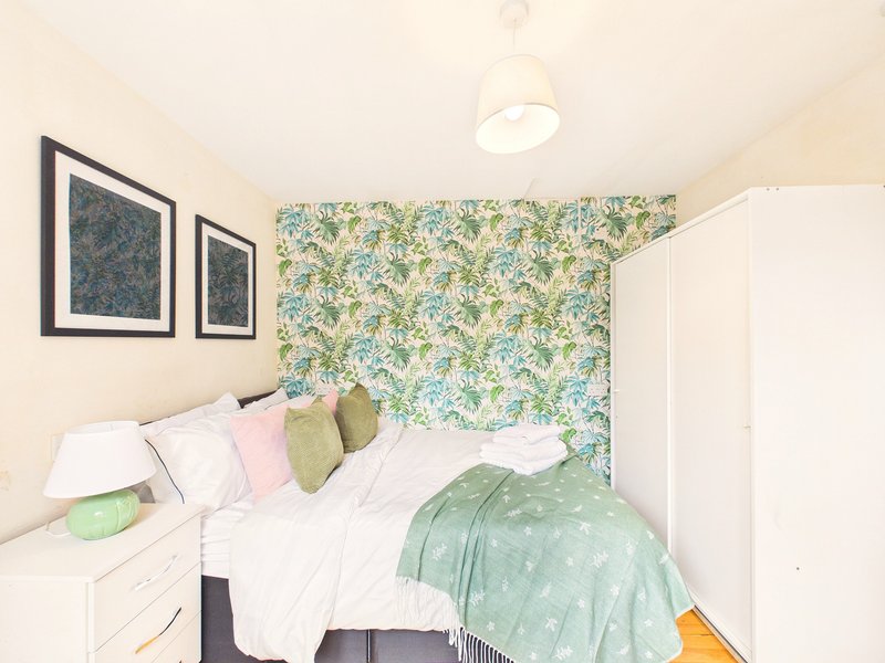 Compact bedroom with double bed, floral accent wall, framed artwork, and white storage furniture