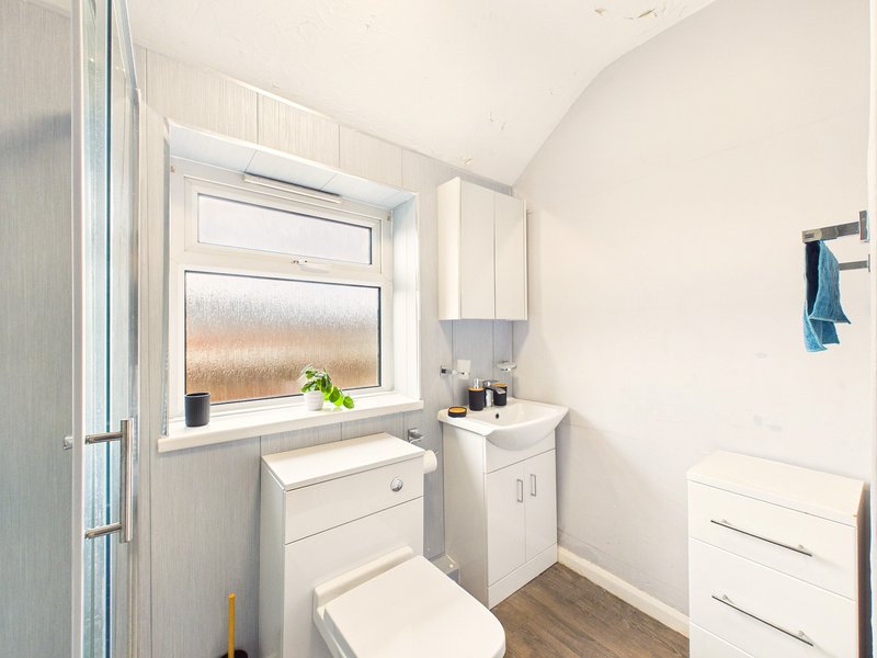 Small bathroom with white vanity, toilet, window, and wooden flooring
