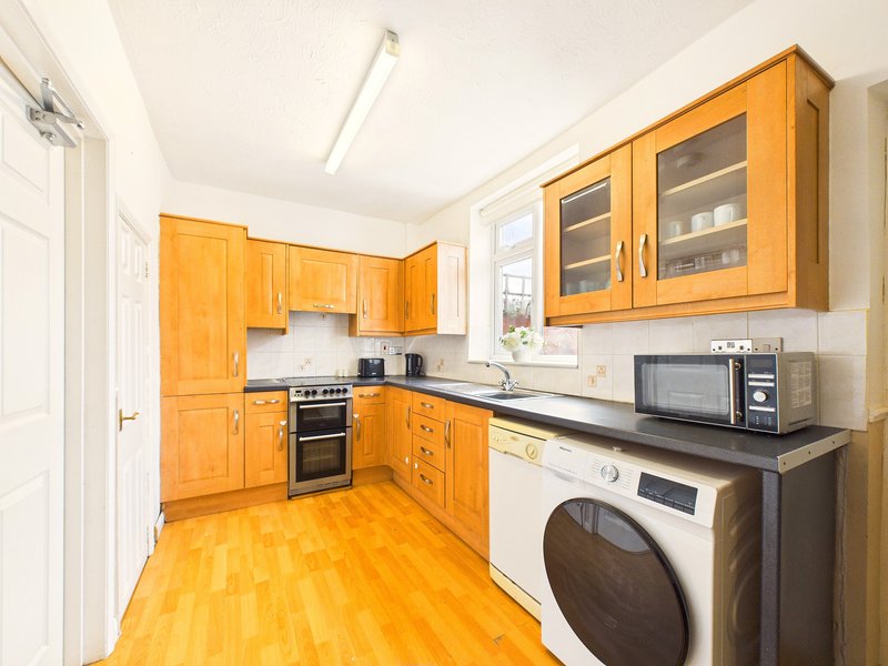 Kitchen with wooden cabinets, built-in oven, microwave, washing machine and wooden flooring