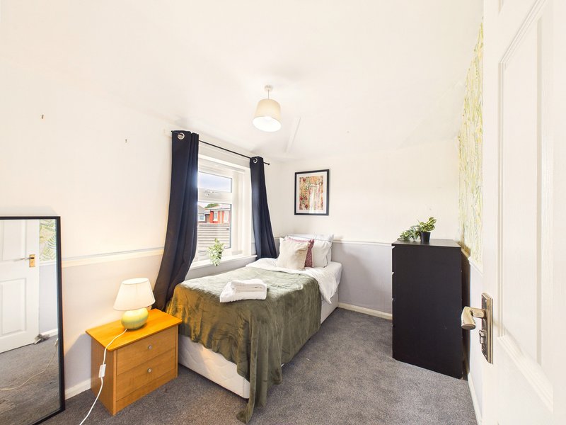 Compact bedroom with single bed, yellow wooden bedside table, black curtains and ceiling pendant light