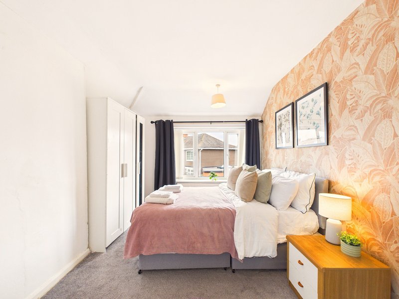 Compact bedroom with double bed, patterned wallpaper, bedside lamp and window
