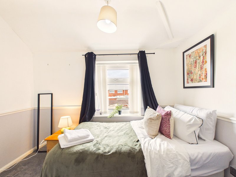 Bedroom with double bed, white pillows, dark green bedding, window with black curtains and street view