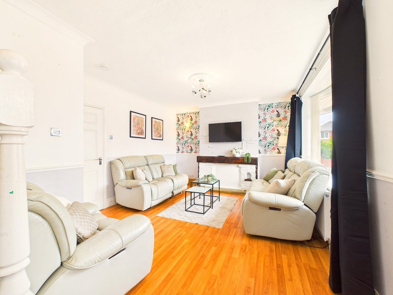 Bright living room with cream armchairs, orange wooden floor, TV and framed wall art