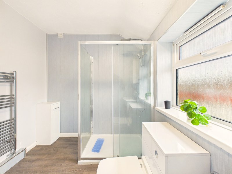 Modern bathroom with walk-in shower, white vanity, toilet, and window with plant