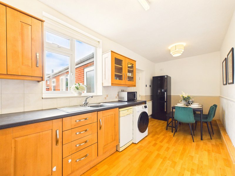 Modern kitchen with wooden cabinets, washing machine, dining table with turquoise chairs and window overlooking street