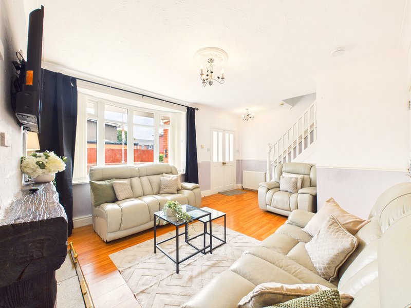 Bright living room with cream sofas, wooden floor, TV, staircase and large windows